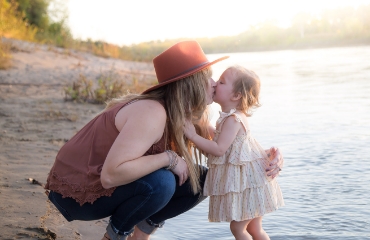 mom and little girl kissing by a river