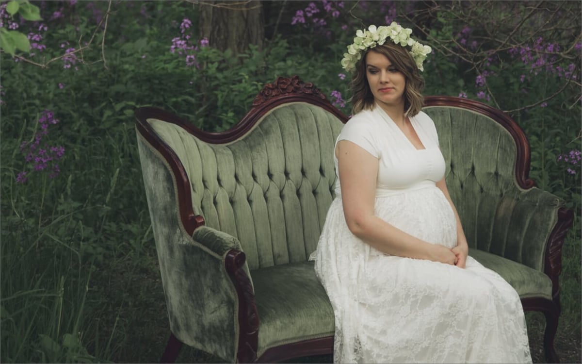 pregnant woman in white dress on vintage couch wearing flower crown