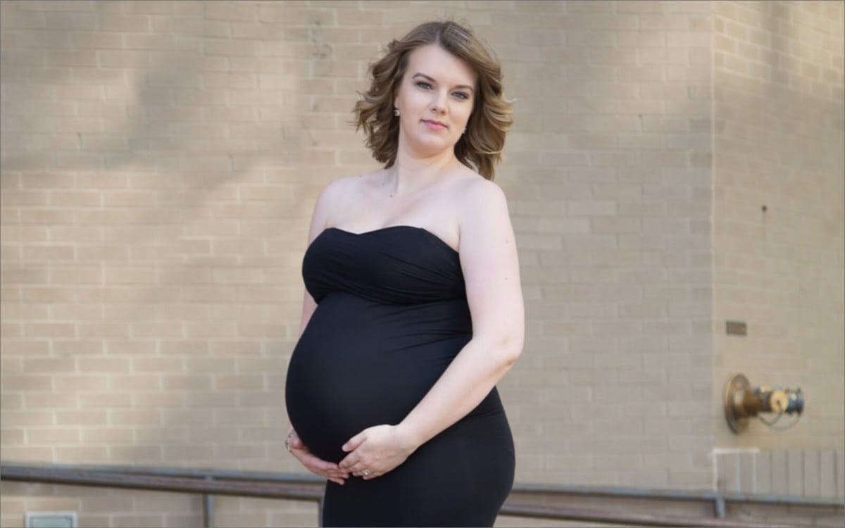 pregnant woman wearing black dress in front of brick wall